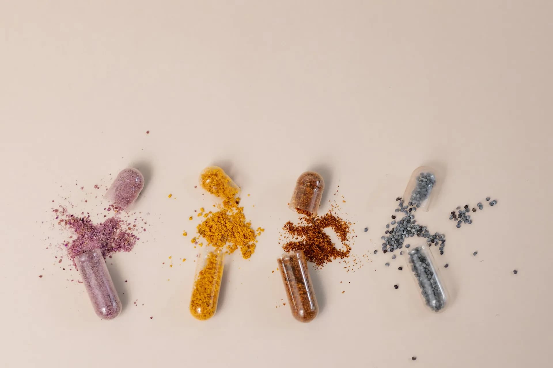 Açılmış kapsüllerin içindeki renkli vitamin ve mineral tozlarının sıra hâlinde dizildiği fotoğraf